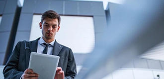 Mann im Anzug liest Unterlagen vor grauem Gebäude mit Fenstern.