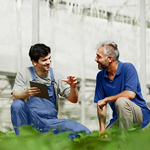 Two men in casual clothes are talking outside; one is holding a notebook.