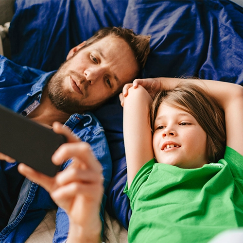 Man and child lying next to each other and looking at a smartphone together.