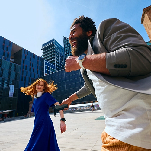 Man with smartphone and woman in casual clothes smile in a square with modern buildings.
